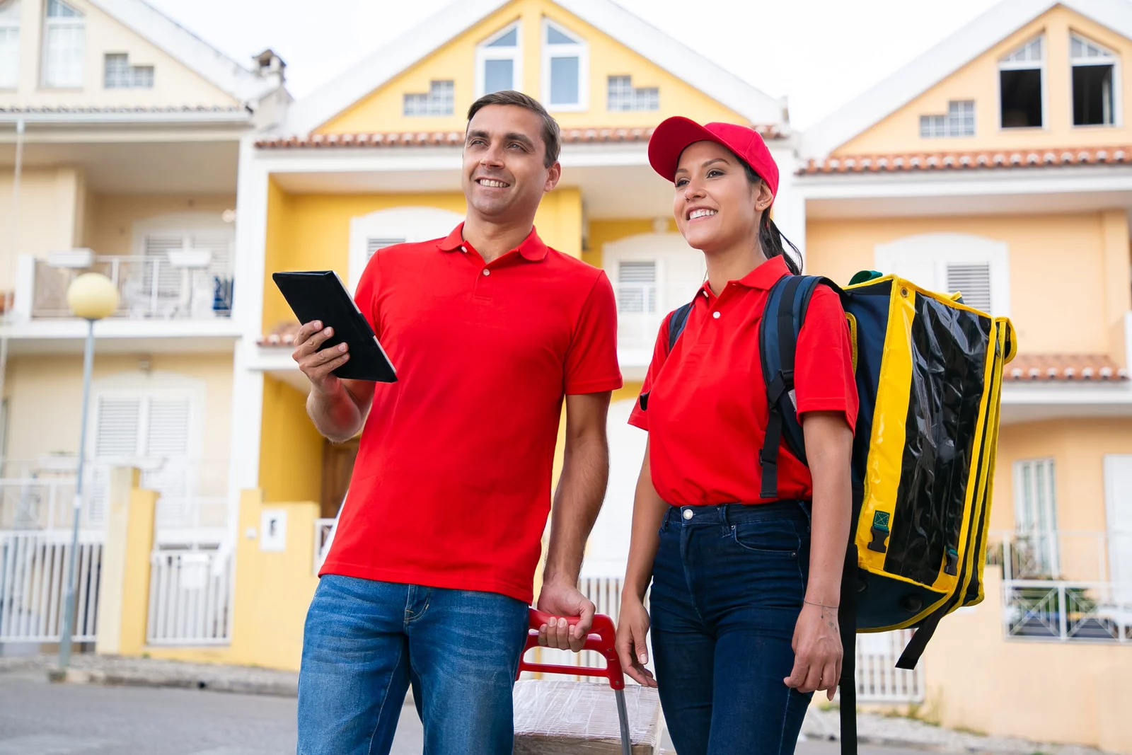 smiling post workers standing looking house address tablet two happy couriers delivering order thermal bag wearing red shirts delivery service online shopping concept scaled 1